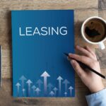 Peak Leasing Season Preparation Essentials: A hand holding a pencil next to a blue leasing brochure, a smartphone, and a cup of coffee on a wooden table.