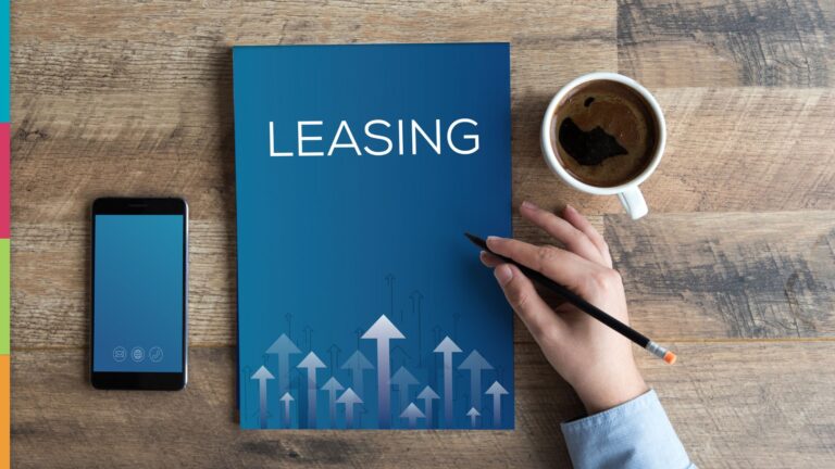 Peak Leasing Season Preparation Essentials: A hand holding a pencil next to a blue leasing brochure, a smartphone, and a cup of coffee on a wooden table.