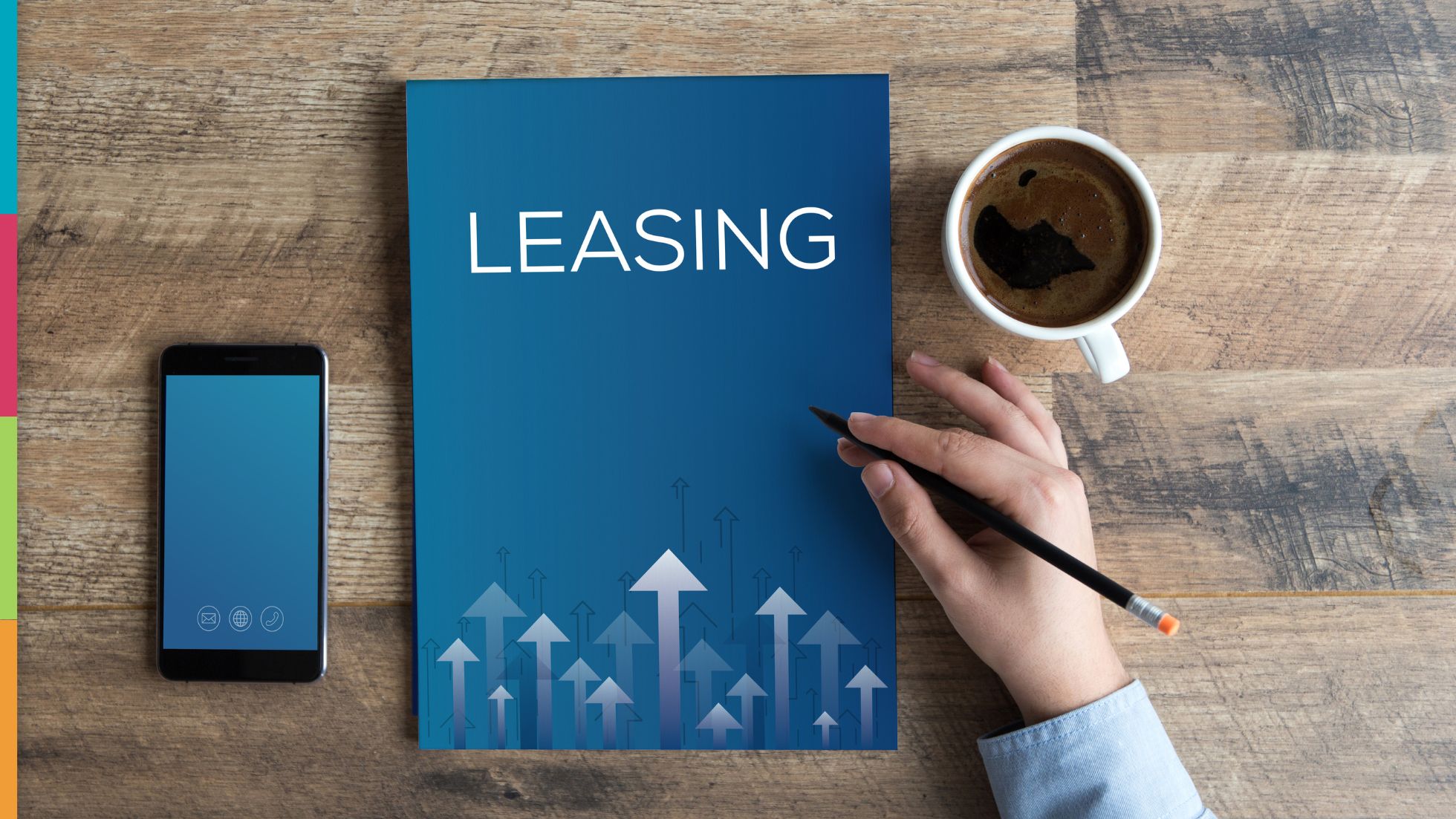 Peak Leasing Season Preparation Essentials: A hand holding a pencil next to a blue leasing brochure, a smartphone, and a cup of coffee on a wooden table.