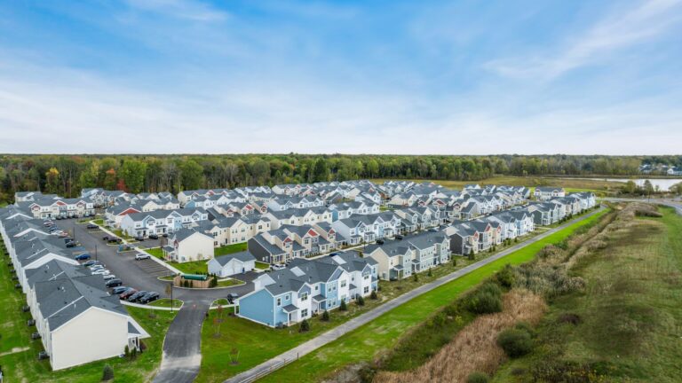 Aerial view of Aspen Heights Buffalo, a modern student housing community in Upstate New York featuring rows of colorful townhome-style apartments surrounded by greenery and trees.