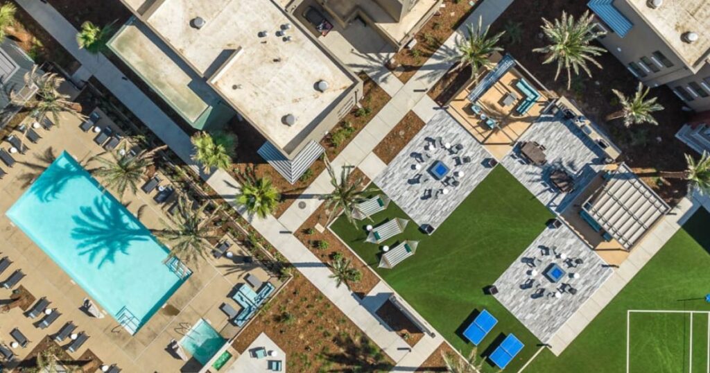 Aerial view of Merced Station in Merced, California, showcasing the student housing community’s outdoor amenities including a swimming pool, lounge areas, palm trees, and green spaces designed for relaxation and recreation.