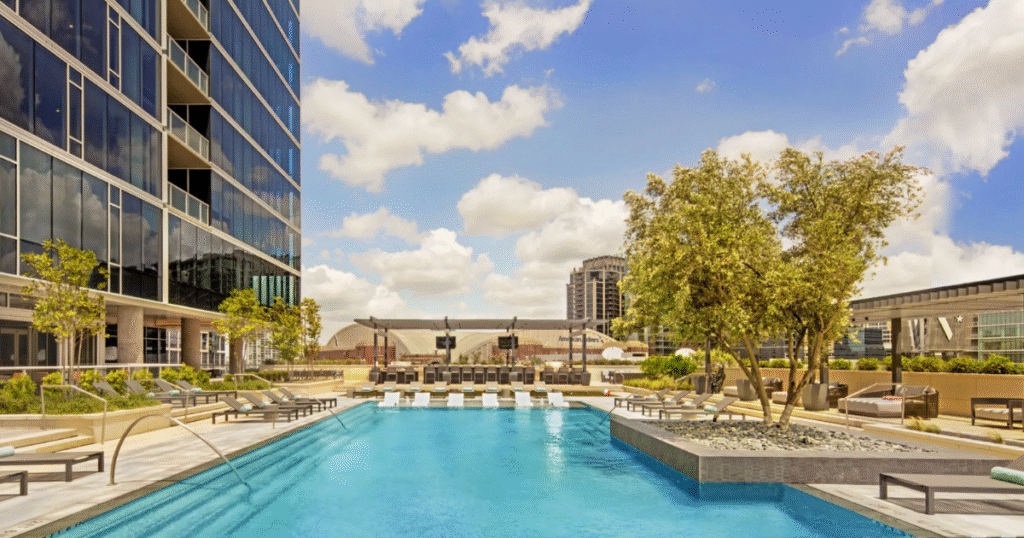 Rooftop pool deck at The Victor luxury high-rise in Dallas, featuring a modern pool, lounge seating, landscaped terraces, and skyline views under a bright blue sky.