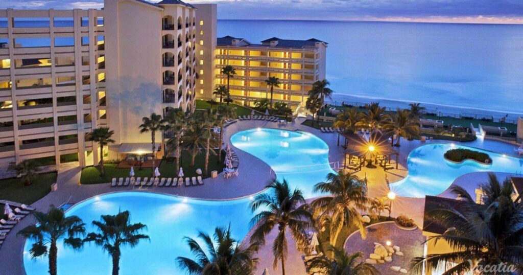 Oceanfront Vacatia resort with illuminated pool and palm trees at sunset