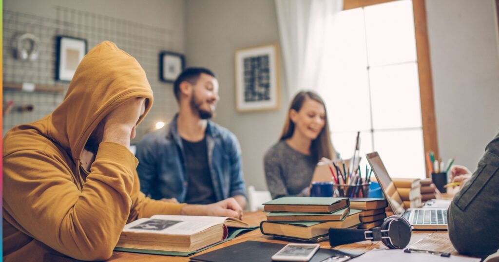 Student housing residents studying together with books and laptop while one student looks frustrated, highlighting shared printing and study challenges