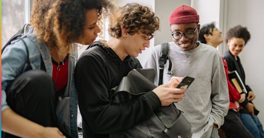 College students standing together using smartphones and talking in a shared off-campus housing space, reflecting social and everyday student life