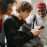 College students standing together using smartphones and talking in a shared off-campus housing space, reflecting social and everyday student life