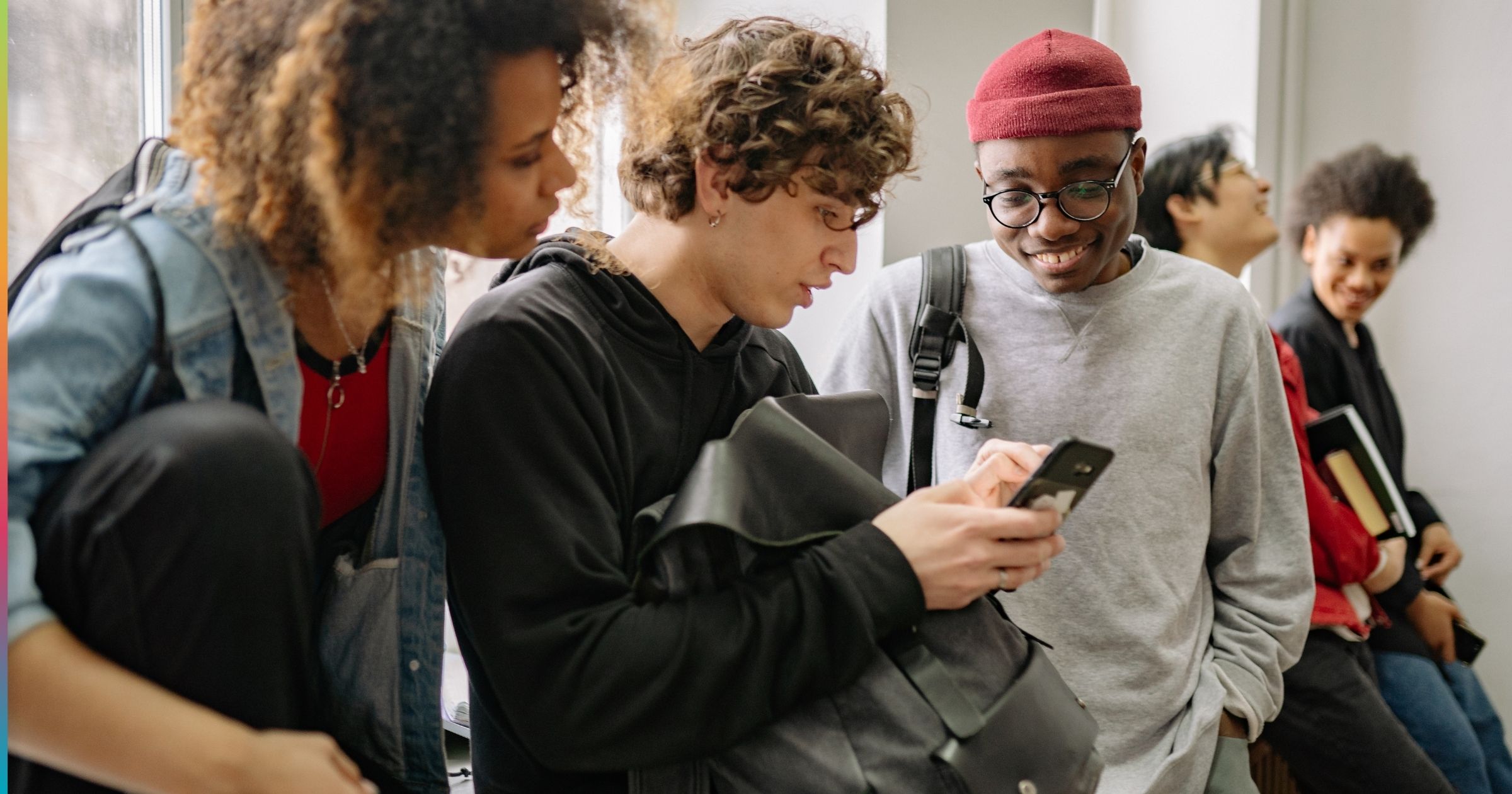 College students standing together using smartphones and talking in a shared off-campus housing space, reflecting social and everyday student life