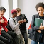 Student holding notebooks walking through a student housing building while other students use phones in the background, highlighting different student needs and daily routines