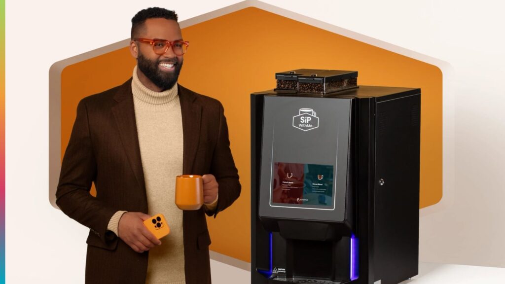 Hotel guest holding an orange coffee mug beside a SipWithMe bean-to-cup machine
